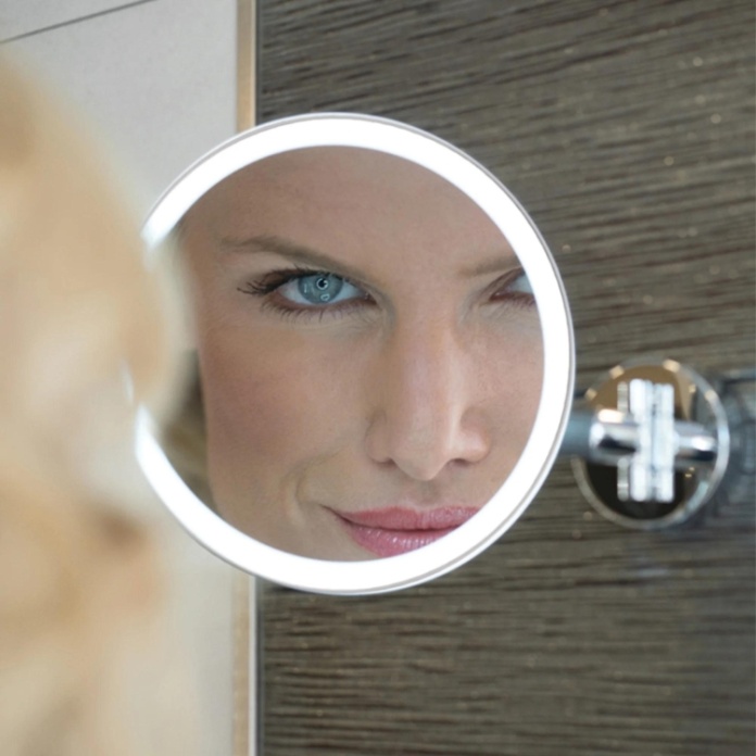Product Lifestyle image of a woman checking her reflection in the HIB Eclipse Round LED Magnifying Mirror